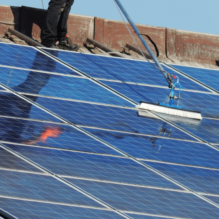Arbeiter reinigt Solarpanel auf einem Dach unter klarem Himmel.