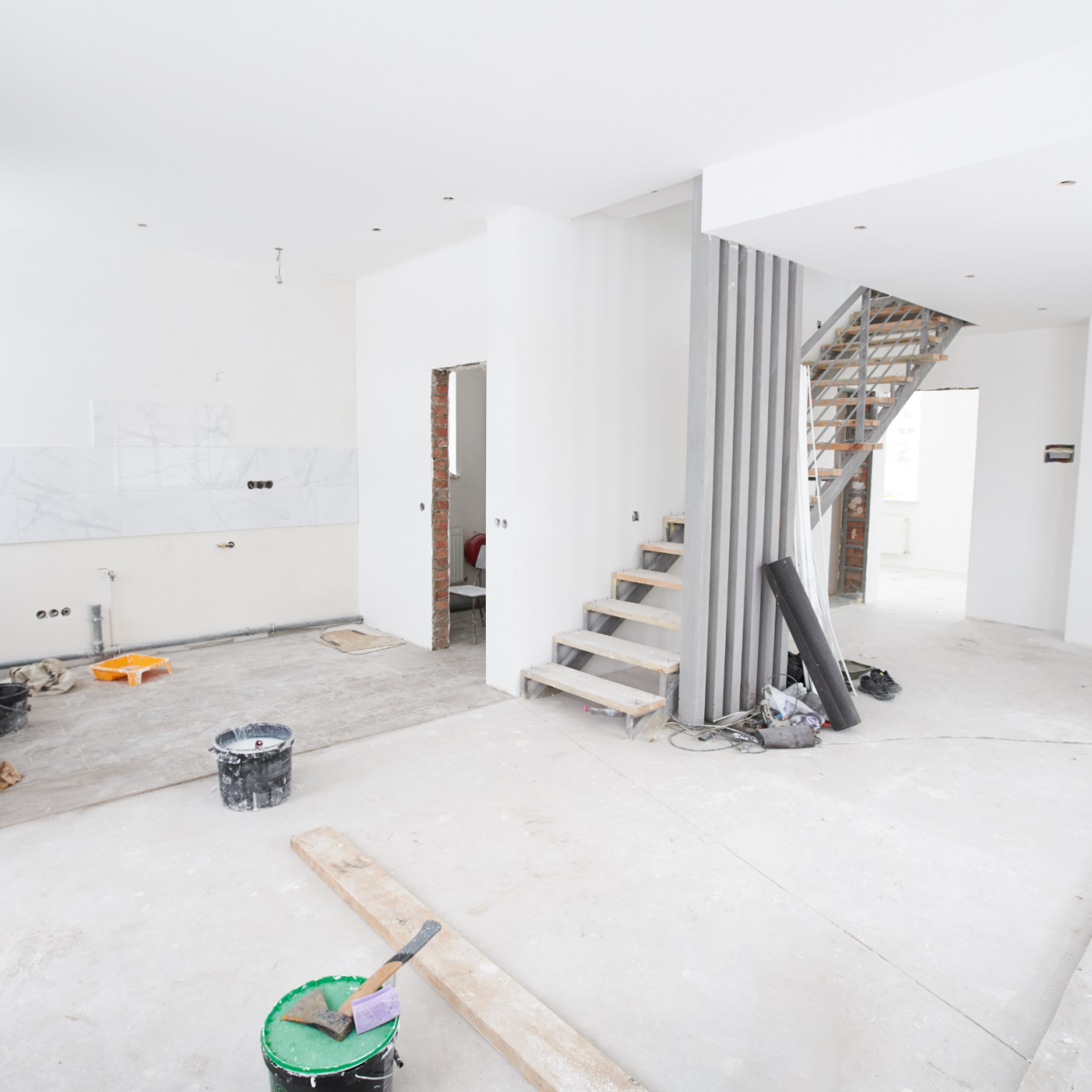 Rohbau eines modernen Raums mit Treppe und Baustellenmaterialien.